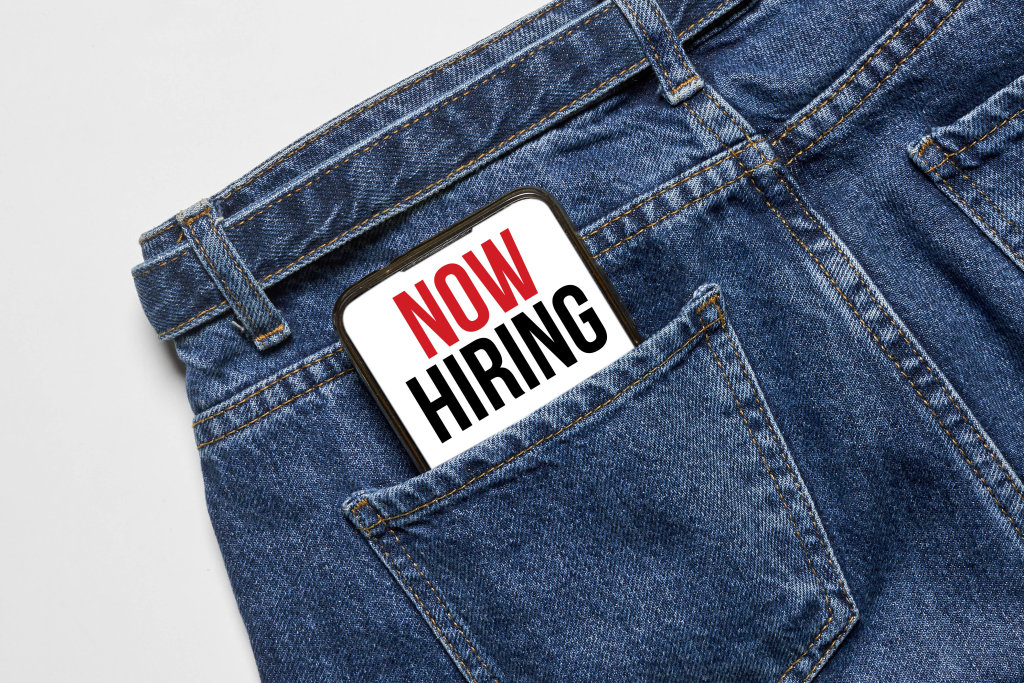 Now hiring phrase on mobile phone screen in the pocket of jeans