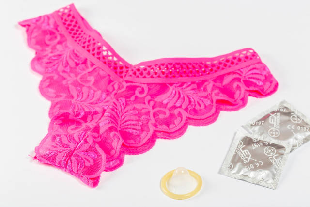 Pink womens panties and condoms on white background