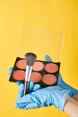 Make-up artist in protective medical gloves holding brush and blush