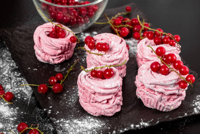Homemade fruit marshmallow with red currant berries and powdered sugar on a dark background