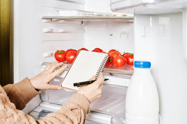 Close-up shot of female checking products in the fridge and making a shopping list