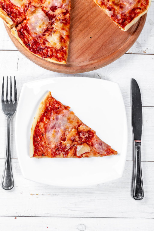 Pizza on a wooden kitchen tray and a piece on a white plate with Cutlery
