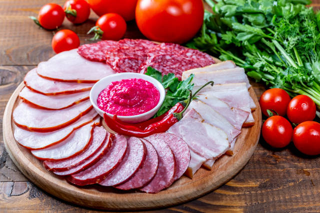 Wooden kitchen Board with sliced smoked sausages, salami, ham and meat with sauce on wooden table