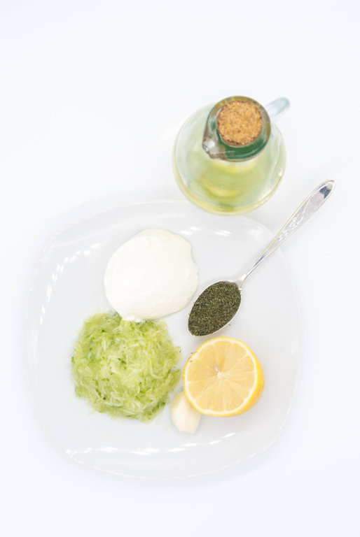 Top view of ingredients for Tzattziki sauce_grated cucumber, lemon juice, oil, sour cream and dill
