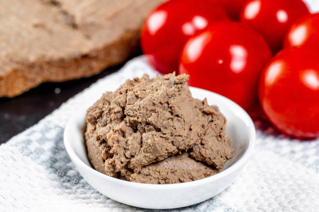 Close-up of liver pate in white bowl with tomatoes behind
