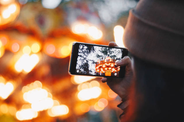 Girl taking picture with smartphone of lunapark. Colorful blurry background.