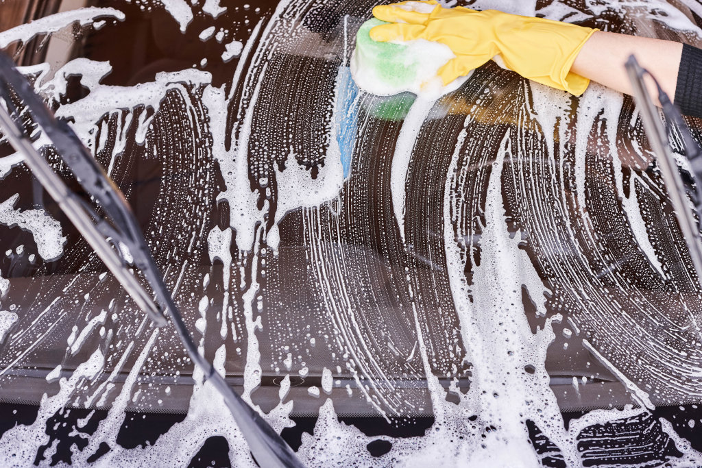 A person washing dirty windshield of car with sponge