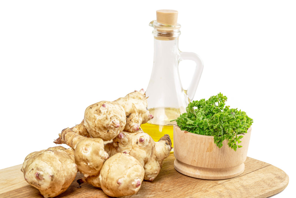 Jerusalem artichoke on a wooden cutting board with oil and parsley
