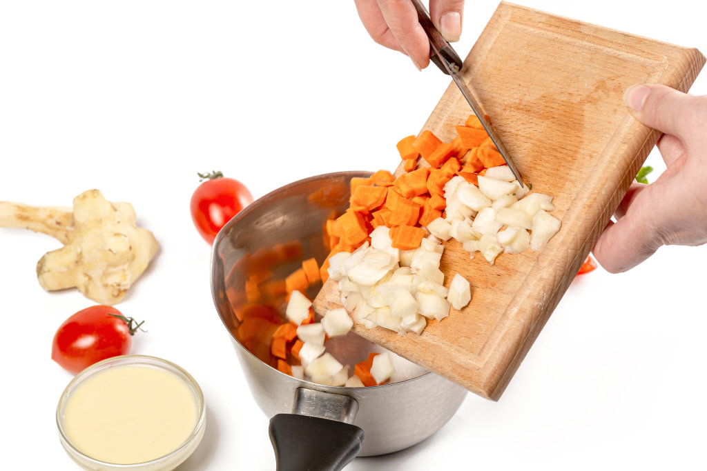 Womans hands pouring chopped vegetables into a saucepan