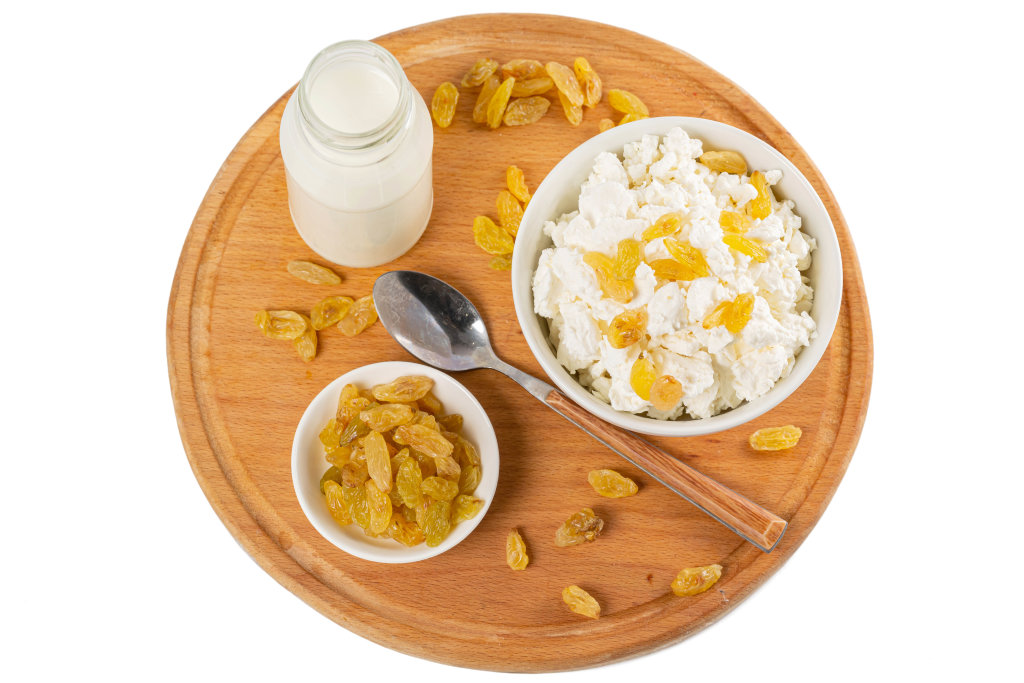 Top view, a bowl of cottage cheese with raisins on a wooden round board with milk