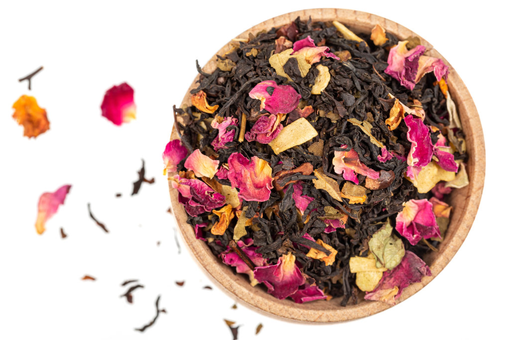 Dry black tea with rose petals in a wooden bowl, top view