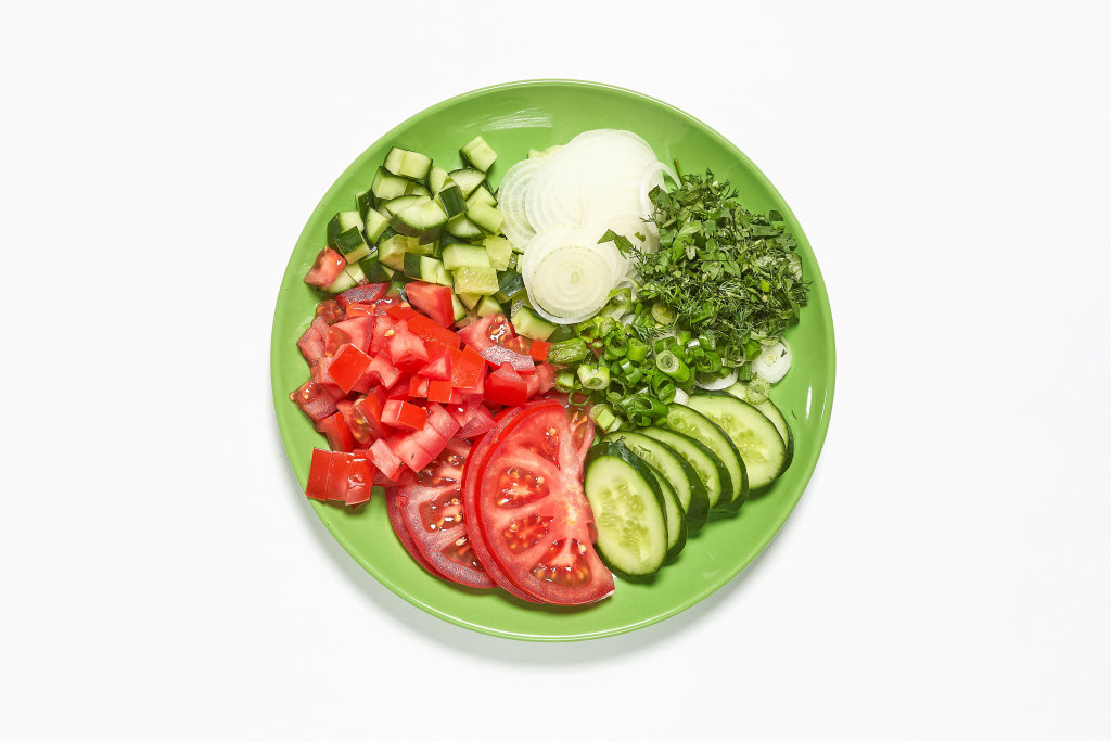 A plate of sliced tomatoes, cucumbers, onions and greens