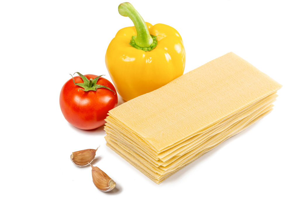 Dry lasagna sheets with garlic, bell pepper and tomato on a white background