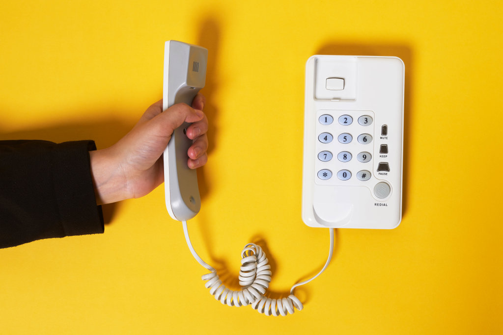 Hand holds classic telephone handset over bright yellow background