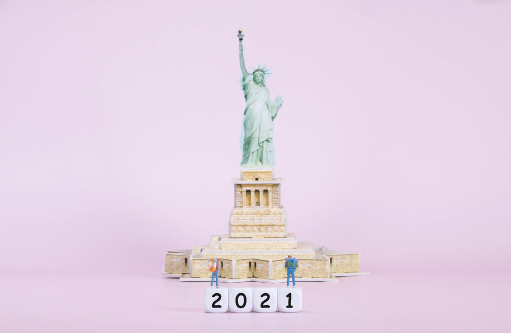 Two travelers standing on blocks with 2021 text in front of Statue Of Liberty