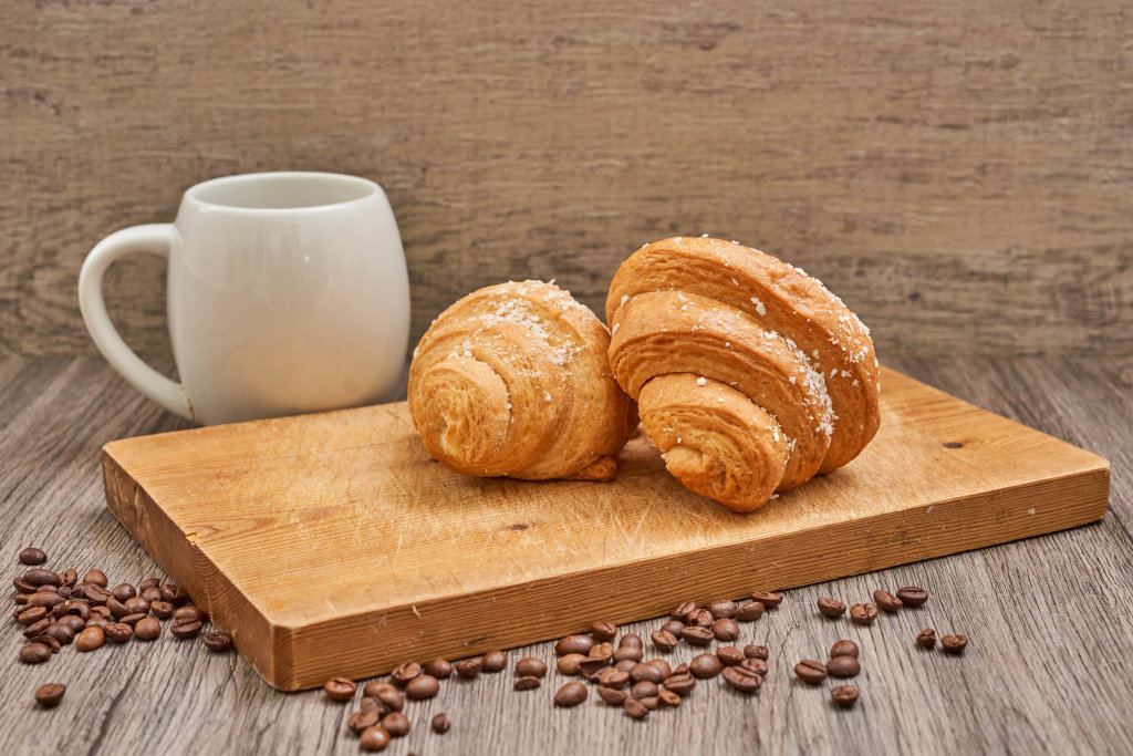 Coffee cup and raw coffee beans with tasty croissants on the wooden cutting board