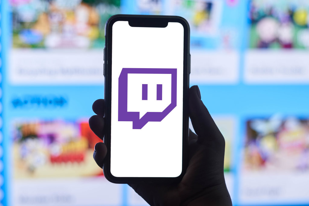 A person holds a smartphone with Twitch application logo over Games Web Portal in the background