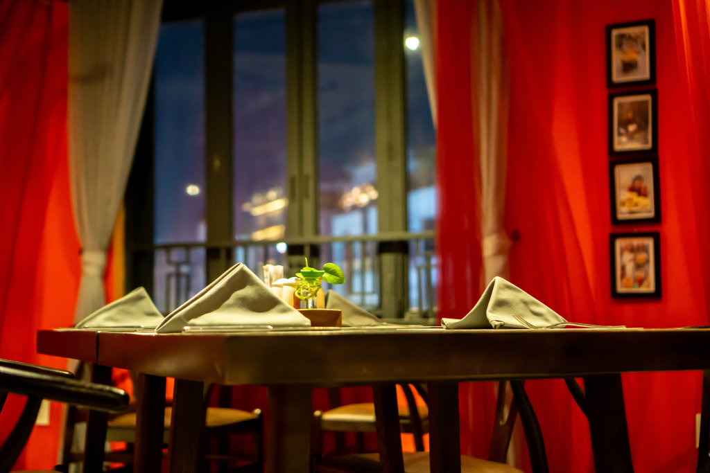 Beautifully Set Table with Cutlery, Napkin and a Small Table Plant at a Middle Eastern Restaurant with White and Red Curtains in the Background