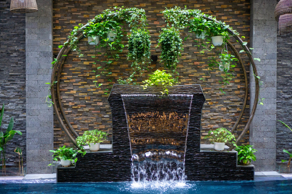Holzbogen mit Hängepflanzen um einen künstlichen Wasserfall an einem Pool vor einer modernen Ziegel Wand in einem Hotel