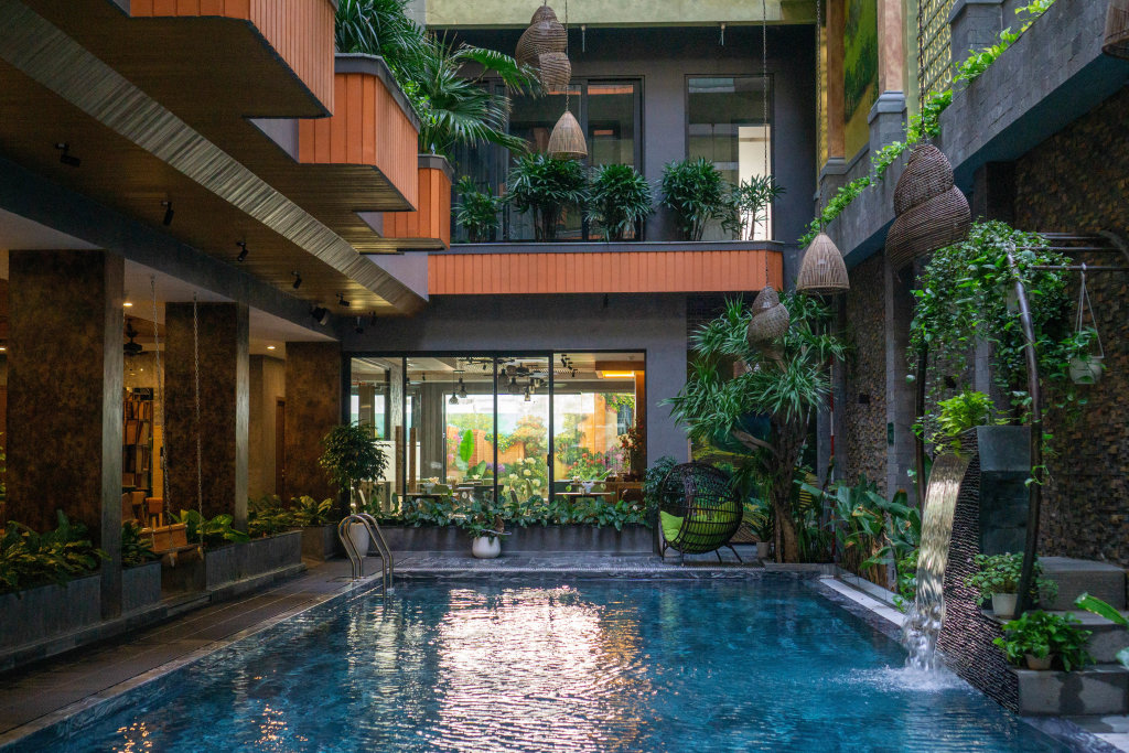 Artificial Waterfall with many Plants next to a Swimming Pool inside a Hotel with a lot of Daylight and modern Architecture