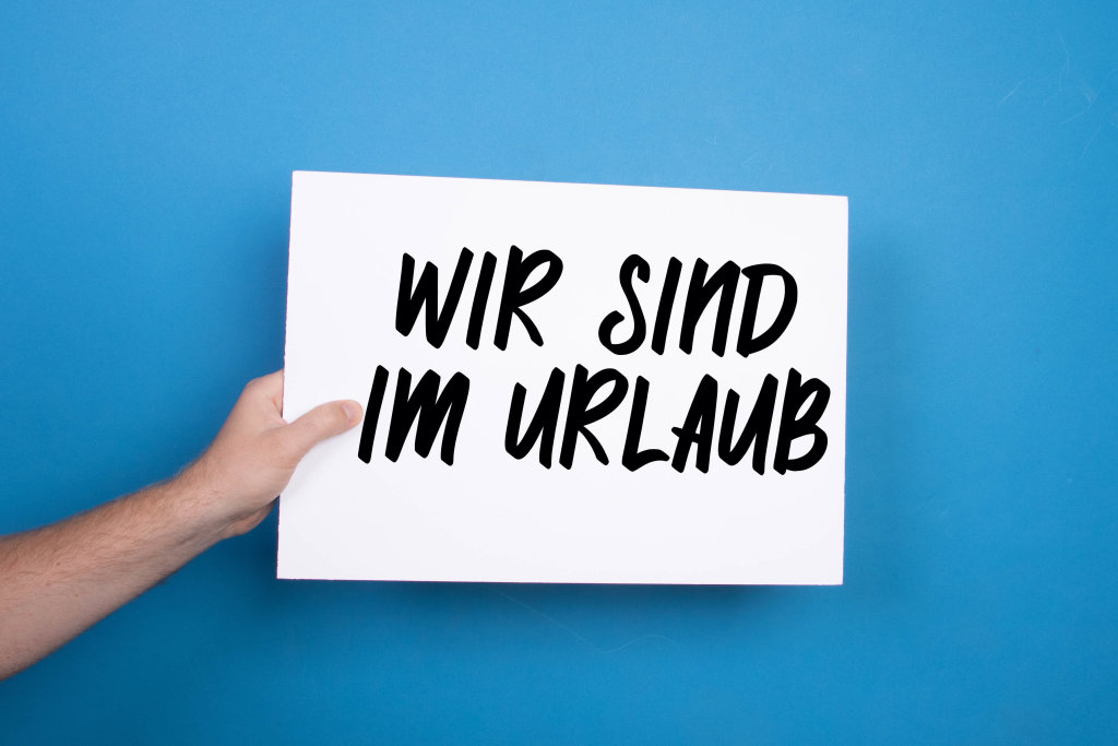 Hand holding white banner with Wir Sind Im Urlaub text on blue background