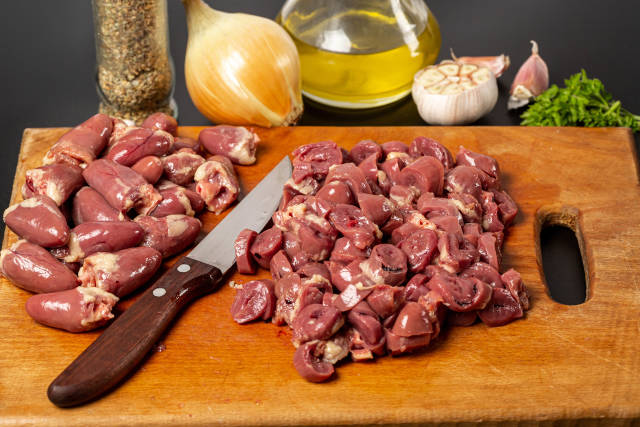 Sliced and whole raw chicken hearts with knife on cutting board