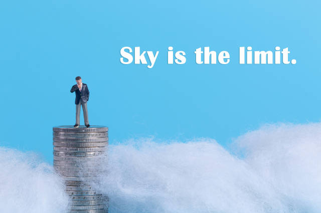 Businessman standing on top of a coinstack surrounded with clouds and Sky is the limit text