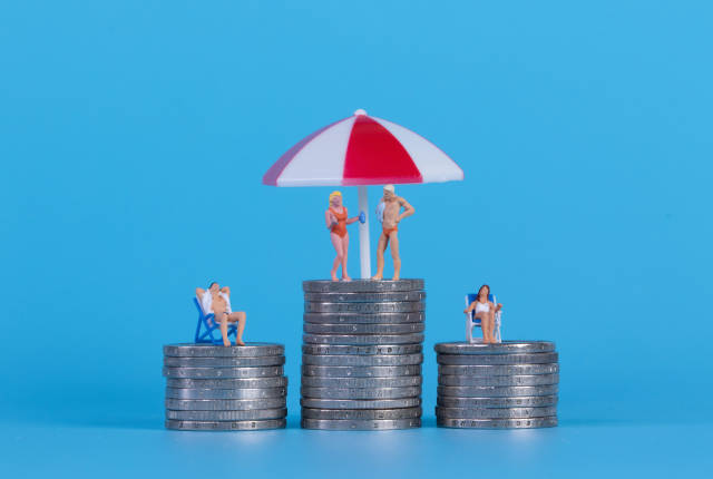 Miniature people in swimsuit on a top of coinstacks with blue background