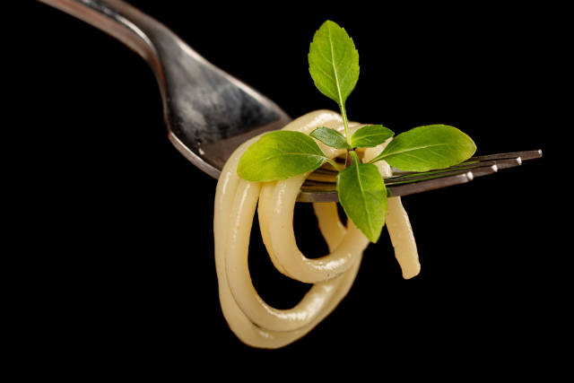 Close-up, spaghetti on a fork with basil leaves, dark background