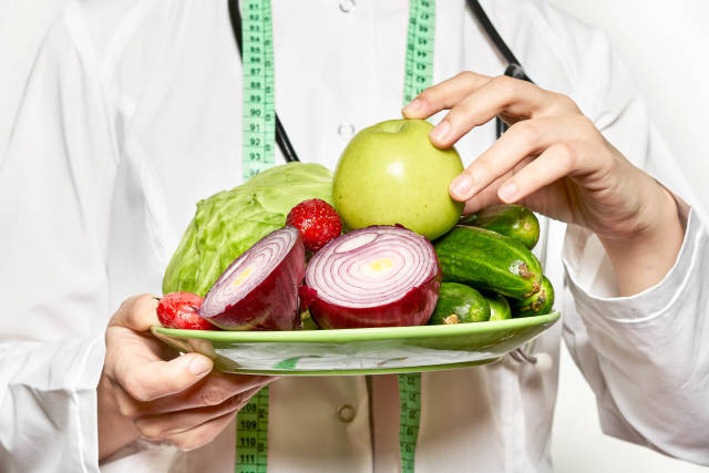 A nutritionist holding a plate full of fresh organic fruits and vegetables for weight loss