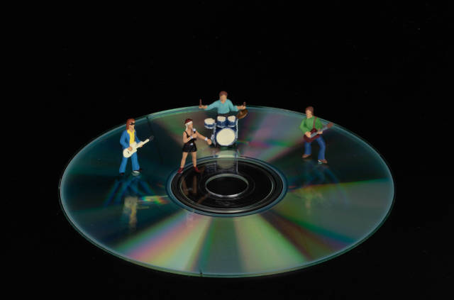 Miniature rock band standing on CD on black background