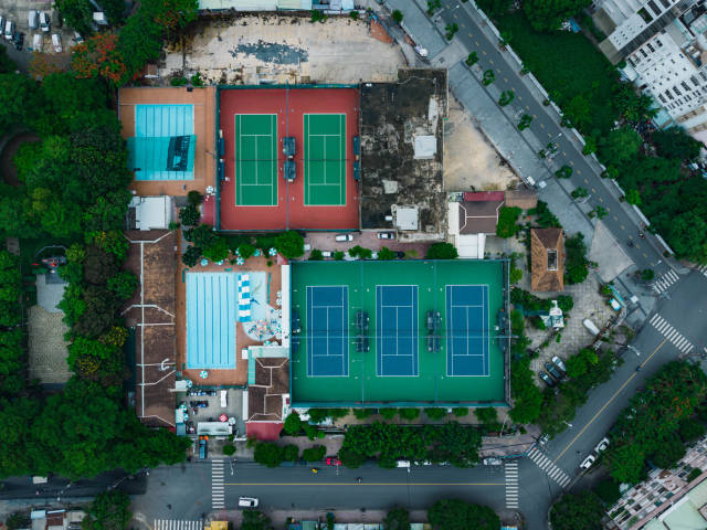 Top View Drone Shot of different colored Tennis Courts with Hardcourt Surface and Swimming Pools next to a Street in District 4 in Ho Chi Minh City, Vietnam