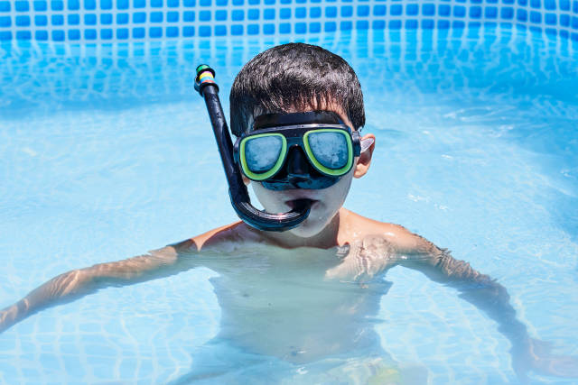 A kid boy of school age wearing mask and snorkel while diving in the pool during summer vacations
