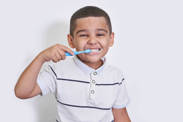 Portrait of little boy brushing teeth on light background