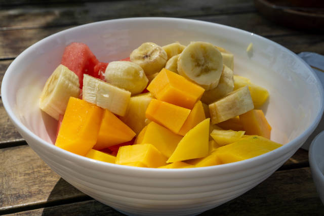 Close Up Food Photo of Mixed Fruit Bowl with sliced Mango, Watermelon, Banana and Pineapple on a Wooden Table in the Sun