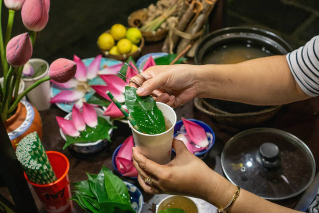 Woman preparing Traditional Herbal Tea with Lotus Flowers, Leaves, Lime and Lemongrass in a Paper Cup with Paper Straw in Hoi An, Vietnam