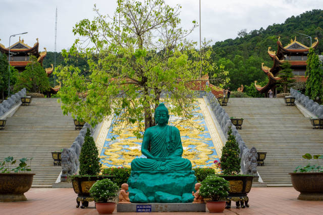 Meditating Buddha Statue with Trees and Plant Pots in front of large Golden Dragon carved in Stone at Truc Lam Ho Quoc Zen Monastery in Phu Quoc, Vietnam