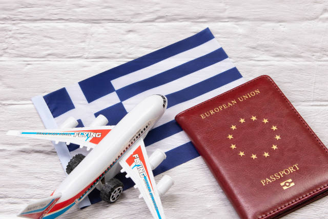 Miniature airplane and passport over flag of Greece