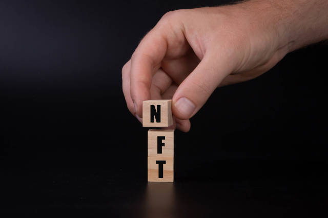 Wooden blocks with NFT text and hand on black background