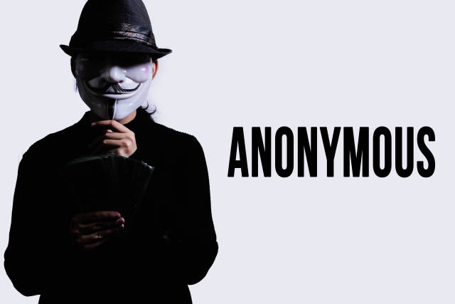 A person in an anonymous mask holding a pile of money. Concept of anonymous donation, hack or robbery