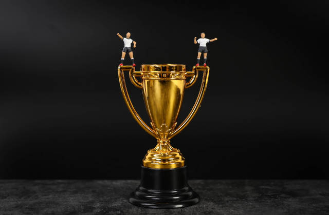 Miniature football players standing on golden trophy