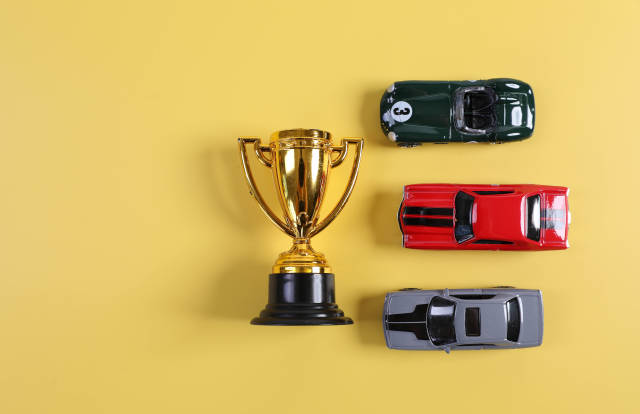 Golden trophy with toy racing cars on yellow background