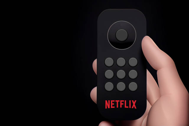 schwarze Fernbedienung in Hand vor schwarzem Hintergrund - Netflix