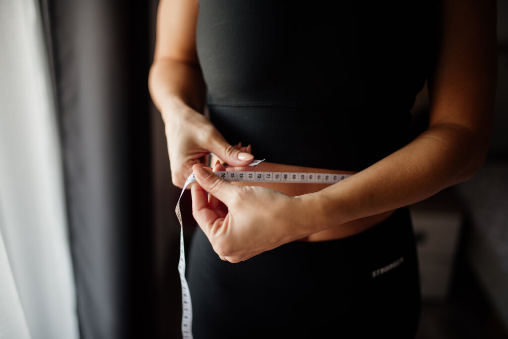 Woman in sportswear measuring her waist with a measuring tape