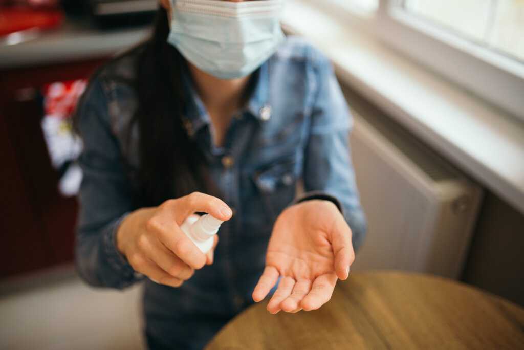 Woman hands using antiseptic spray with protective medical mask.