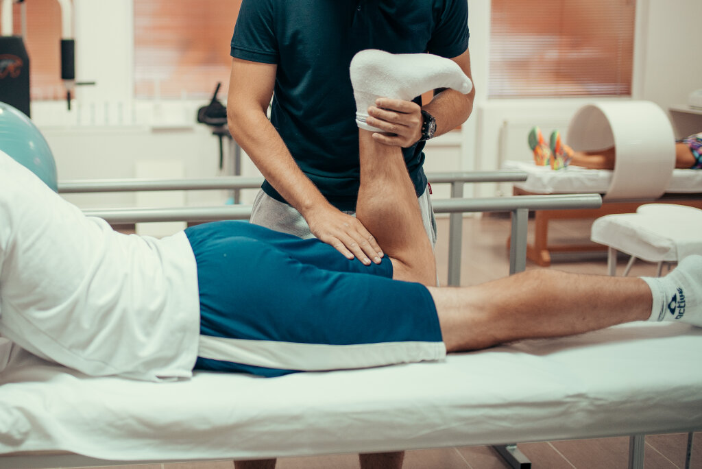 Physiotherapist working examining treating injured leg of male patient.