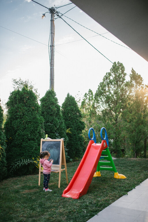 Young girl standing next to a slide and a chalkboard in the backyard.