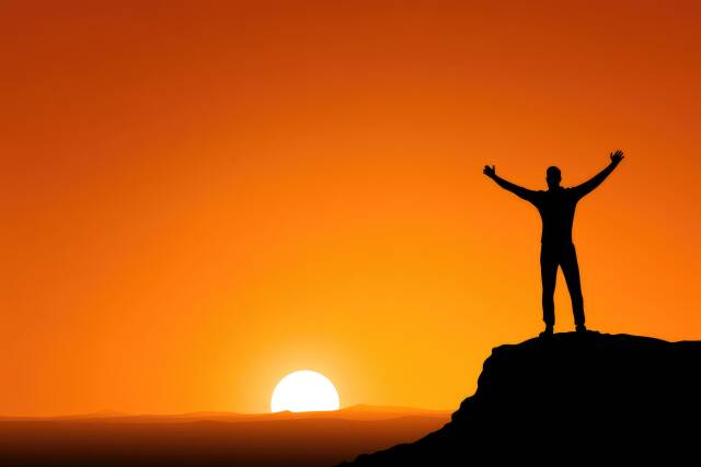 Mensch reißt bei einem Sonnenuntergang die Arme in die Luft