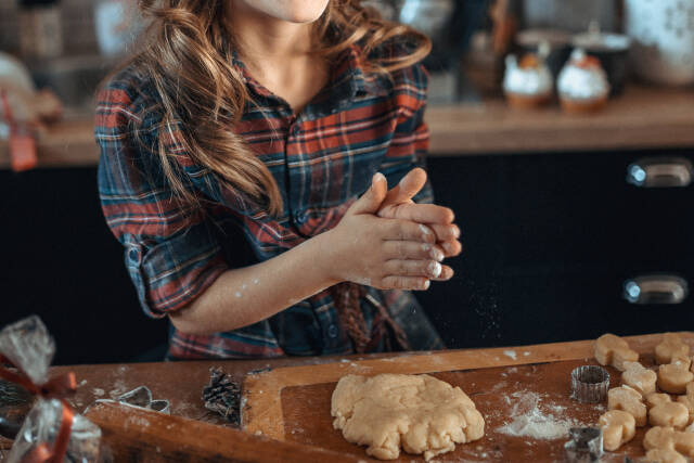 Young girl with curly hair wearing a plaid shirt holding her hands above the dough