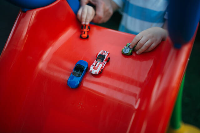 Boy playing with toy cars on the slide and adult supervising.